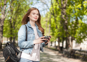 Cute young attractive woman tourist in denim jacket with retro camera in the city