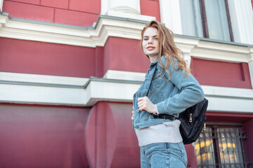 Stylish sexy woman in denim clothes and backpack in city