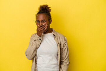 Young african american woman isolated on yellow background covering mouth with hands looking worried.