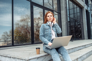 Young woman student or freelancer sits on the stairs with a laptop