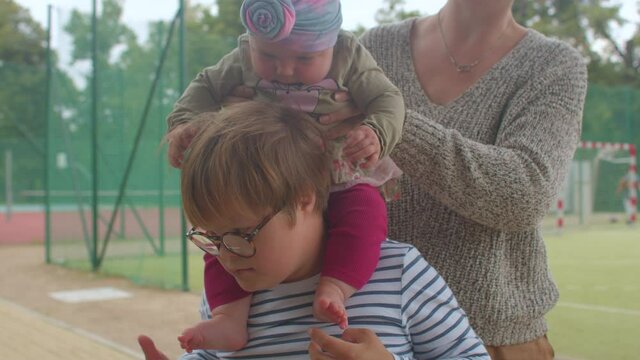 A toddler girl sits on the shoulders of a down syndrome teenager. Tactile sensations of communication. Increasing the sensitivity of the child.