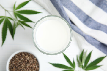 Obraz na płótnie Canvas Glass of fresh hemp milk, seeds and leaves on white table, flat lay