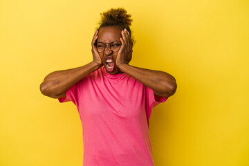 Young african american woman isolated on yellow background covering ears with hands trying not to hear too loud sound.