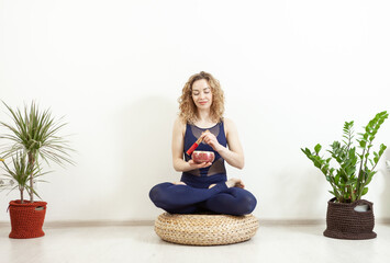Woman yogi plays on Tibetan singing bowl. Young woman meditating in yoga studio. Yoga and healthy...