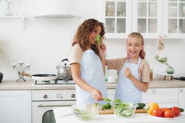 Mother and daughter playing and having fun with vegetables in kitchen