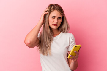 Young russian woman holding a mobile phone isolated on pink background being shocked, she has...