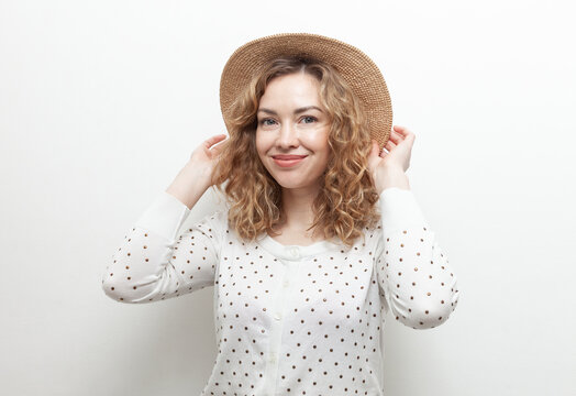 Portrait of cute smiling curly haired Caucasian woman in straw hat on white background