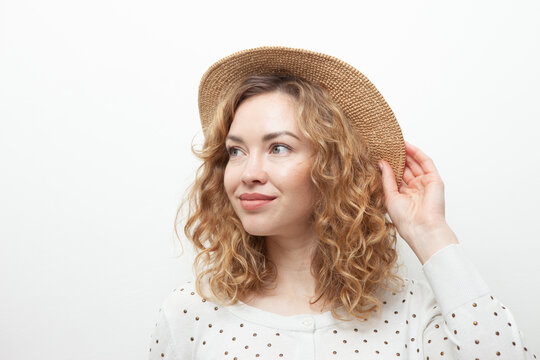 Portrait of cute smiling curly haired Caucasian woman in straw hat on white background