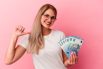 Young russian woman holding bills isolated on pink background feels proud and self confident,...