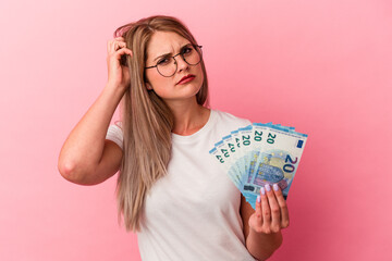 Young russian woman holding bills isolated on pink background being shocked, she has remembered important meeting.