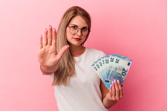 Young russian woman holding bills isolated on pink background standing with outstretched hand showing stop sign, preventing you.