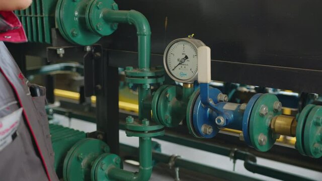 Lever and pressure meter with thin pipes near metal wall in brightly lit plant workshop extreme close view.