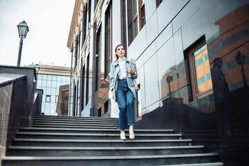 Business woman with laptop quickly descends the stairs of business building. Lifestyle