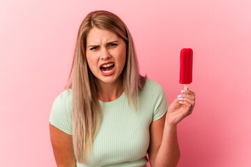 Young russian woman holding an ice cream isolated on pink background screaming very angry and aggressive.