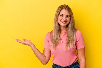 Young russian woman isolated on yellow background showing a copy space on a palm and holding another hand on waist.