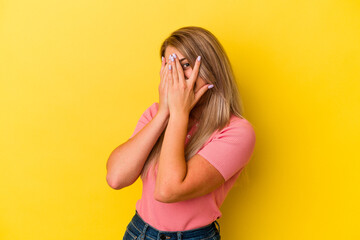 Young russian woman isolated on yellow background blink through fingers frightened and nervous.