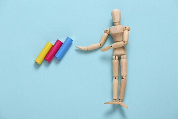 Wooden puppet points to Colored AA batteries on a blue background
