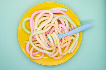 A plate with spaghetti marmalade and a fork on a blue background. Delicious snack.