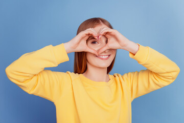 Portrait of funny cheerful girlfriend lady show heart gesture cover eye on blue background