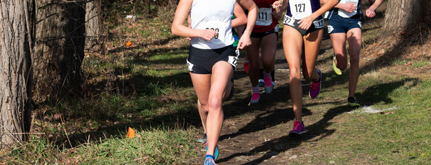 High school girls running out of the woods on a dirt path during a cross country 5K race
