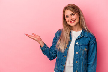 Young russian woman isolated on pink background showing a copy space on a palm and holding another hand on waist.