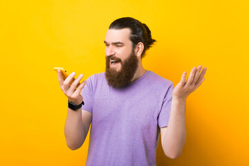 Confused young bearded man is talking to a phone he is holding.