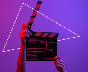 Hand holding film clapper board in neon light with triangle. Cinema industry, entertainment.