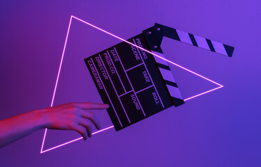 Hand touches film clapper board in neon light with triangle. Cinema industry, entertainment....