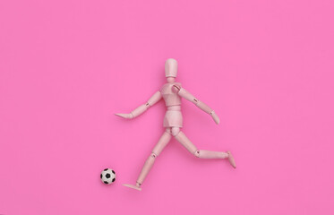 Mini wooden puppet running with a soccer ball on pink background