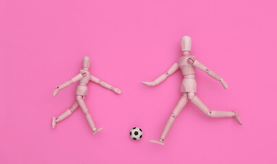 Two wooden puppet playing soccer with a ball on pink background