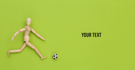 Wooden puppet playing soccer with a ball on green background. Copy space