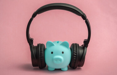 Piggy bank with stereo headphones listening to music on pink background