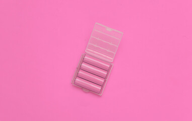 Four yellow AA batteries in plastic box on pink background. Top view