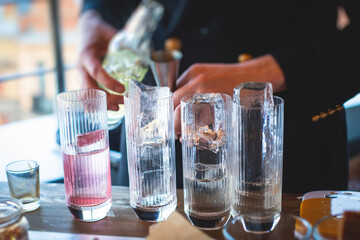 Bartender in front of beautiful row of different coloured alcohol cocktails on a party in a bar, martini, vodka, and others on decorated catering banquet table on open air event