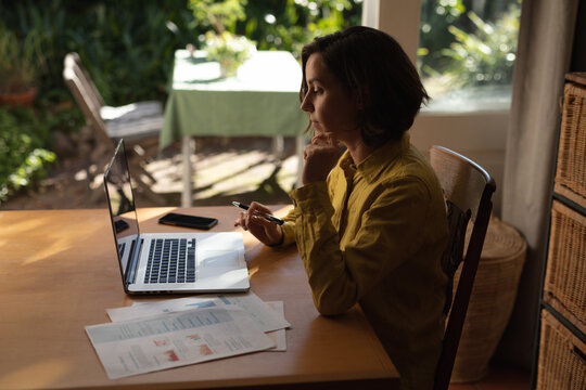 Caucasian woman in living room, sitting at table working, using laptop