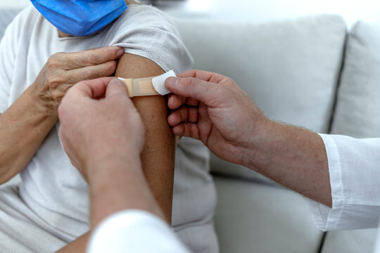 A male doctor puts a band aid on a senior woman's arm after he administered the COVID-19 vaccine injection. Close up image of elderly woman having vaccination. Coronavirus, medical exam, consultation.