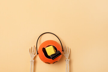 Skeleton Arms Holding Small Jack-O-Lantern Pumpkin Basket with Candy Yellow Background Top View Copy Space