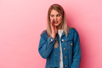 Young russian woman isolated on pink background is saying a secret hot braking news and looking aside