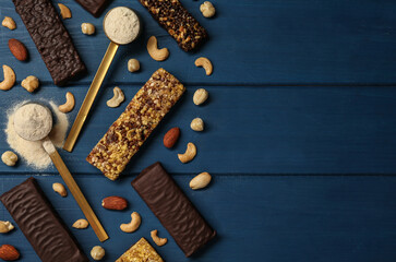 Different tasty bars, nuts and protein powder on blue wooden table, flat lay. Space for text