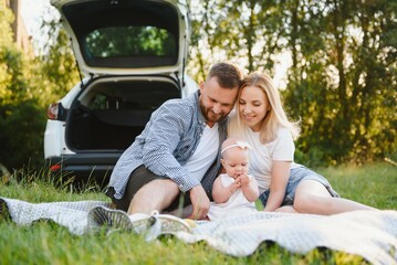 Young family three people in white clothes have picnic. Beautiful parents and daughter travel by car during summer vacation.