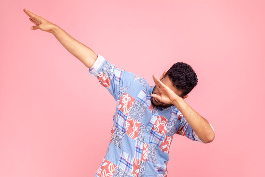 Photo of dark haired man wearing blue casual style shirt showing popular internet meme pose, celebrating success victory, dabbing trends. Indoor studio shirt isolated on pink background.