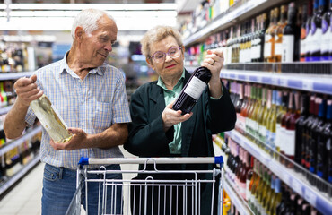 mature couple chooses bottle of wine in alcohol section of supermarket
