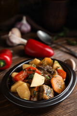 Tasty cooked dish with potatoes in earthenware on wooden table
