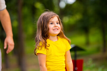 Fototapeta premium Close up photo of a smiling little girl satisfied of being with her dad in the park, they spend nice summer day in the park.