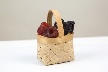 Pieces of handmade soap in the form of raspberries in a wooden basket on a white background