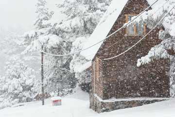 Wooden two floor house with roof covered by snow blurred by snowflakes on snowdrifts