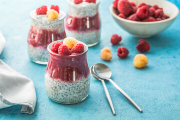 glass jars with chia pudding with raspberry and jam. Bowl of raspberry berry on the blue background.