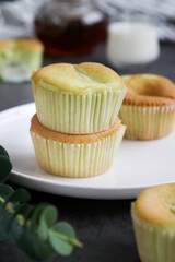 A pile of coconut- pandanus sponge cupcakes muffin on a white plate with a pot of tea and milk in background, it's a fusion aroma and light Asian tropical cake with extract of pandan juice