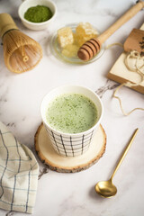 A cup of hot matcha green tea with golden spoon and chasen whisk , honeycomb, its powder in background. Matcha is rich in catechins, a class of plant compounds in tea that act as natural antioxidants