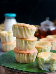 A pile of coconut- pandanus sponge cupcakes with a bite piece lava sauce inside on a banana leaves with pot of milk and tea and black background, it's a fusion Asian tropical cake 